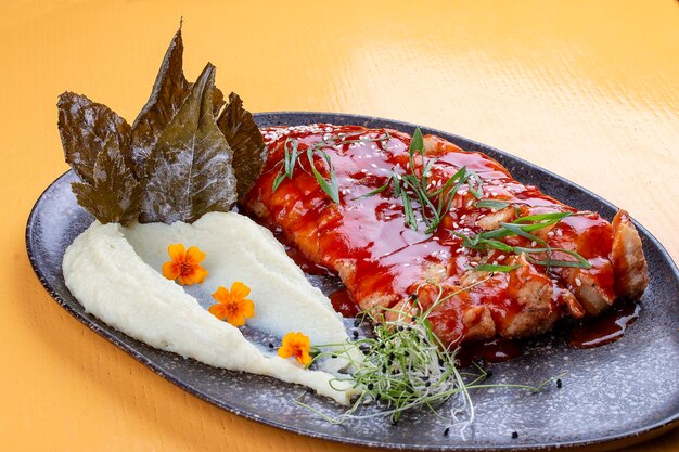 Carpe en sauce chinoise aigre-douce avec purée de pommes de terre et feuilles de vigne Sur un plateau en céramique sombre