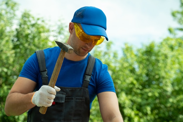 Carpenter enfonce un clou dans une planche de bois en se tenant à l'extérieur