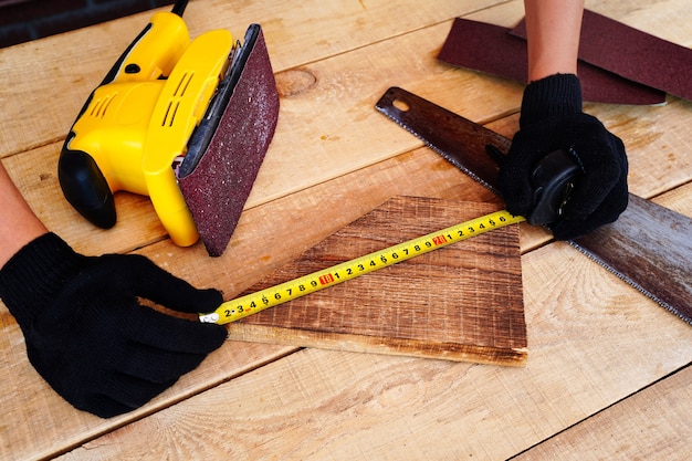 Carpenter mesurant une planche de bois sur le lieu de travail avec des gants fabriquant des produits faits à la main à partir de bois