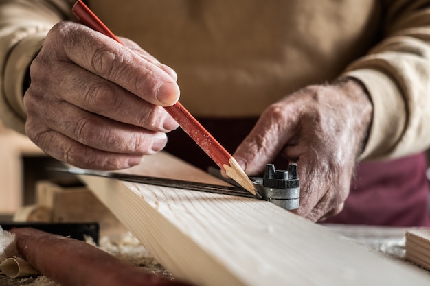 Carpenter mesurant une planche avec un crayon rouge et une règle en métal