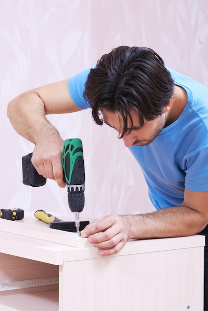 Carpenter recueille des meubles en bois avec une perceuse