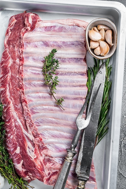 Carré cru non cuit de côtes d'agneau de mouton dans un plat allant au four. Fond blanc. Vue de dessus.