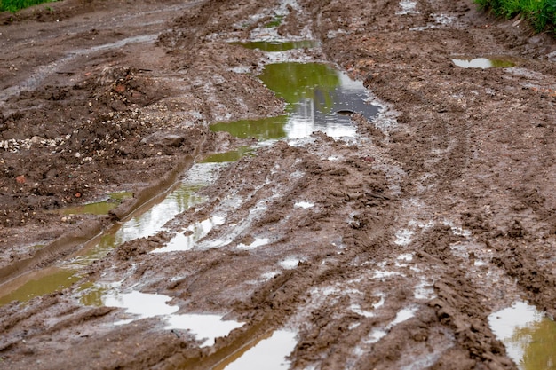 Carrefour de boue d'argile sale avec des flaques d'eau et des traces de pneus en gros plan avec mise au point sélective et perspective linéaire