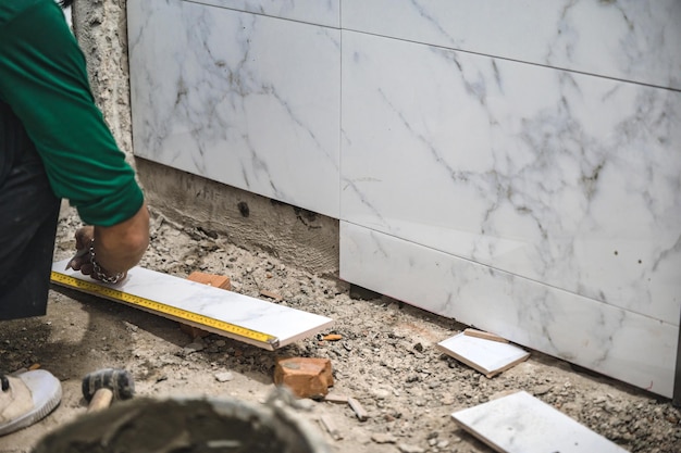 Carreleur mâle à l'aide d'une truelle pose de carreaux de marbre avec du ciment dans la salle de bains Développement de logements Rénovation d'amélioration de l'intérieur