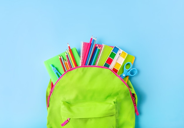 Cartable vert plein de fournitures scolaires sur bleu