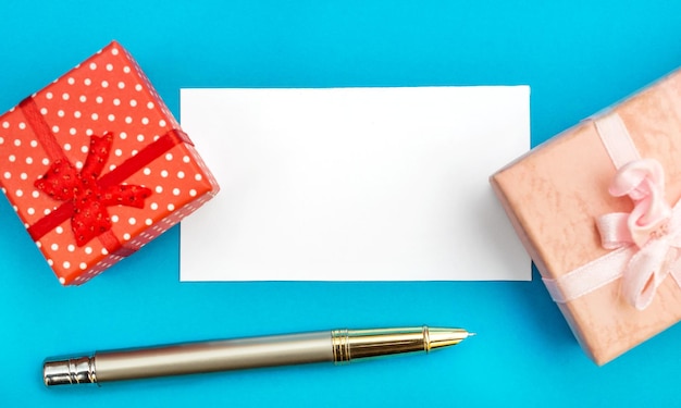 Carte blanche avec des boîtes-cadeaux et un stylo sur bleu Concept de vacances Vue supérieure