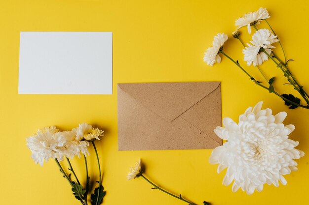 Une carte blanche avec une enveloppe et des fleurs est placée sur un fond jaune