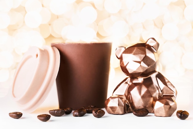 Carte-cadeau avec un ours au chocolat et une tasse de café sur fond doré de lumières de Noël bokeh