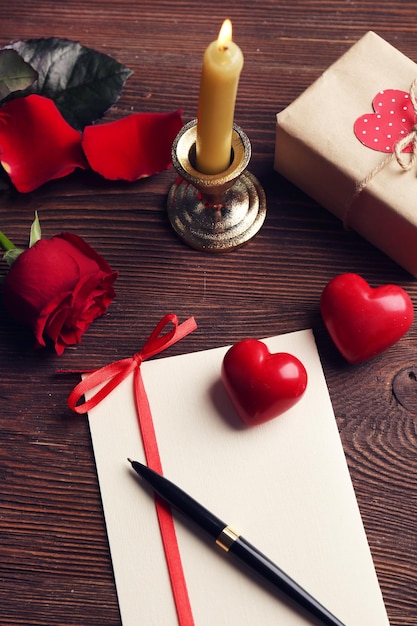 Carte-cadeau pour la Saint-Valentin avec boîte stylo rose rouge et bougie sur fond de bois