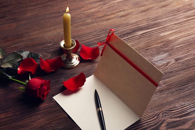 Carte-cadeau pour la Saint-Valentin avec stylo pétales rouges et bougie sur fond de bois