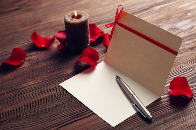 Photo carte-cadeau pour la saint-valentin avec stylo pétales rouges et bougie sur fond de bois