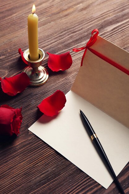 Carte-cadeau pour la Saint-Valentin avec stylo pétales rouges et bougie sur fond de bois