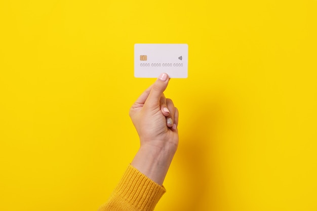 Carte de crédit blanche en main féminine, carte avec puce électronique sur fond jaune