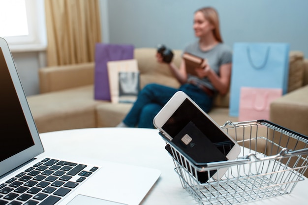 Carte de crédit, smartphone et ordinateur portable, femme assise sur le canapé avec des sacs