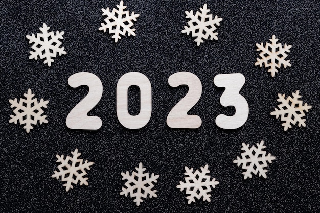 Carte du Nouvel An 2023 Chiffres en bois de l'année et flocons de neige sur fond étoilé noir brillant