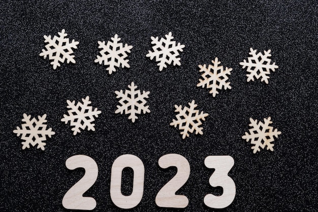 Carte du Nouvel An 2023. Numéros en bois de l'année et flocons de neige sur fond étoilé noir brillant.