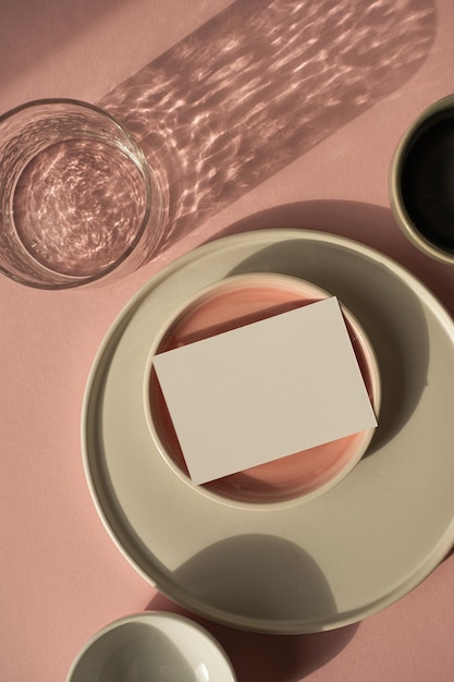 Carte de feuille de papier vierge avec espace de copie de maquette sur fond rose poussiéreux Modèle de marque d'entreprise bohème esthétique Assiettes en céramique et verre avec des ombres scintillantes du soleil