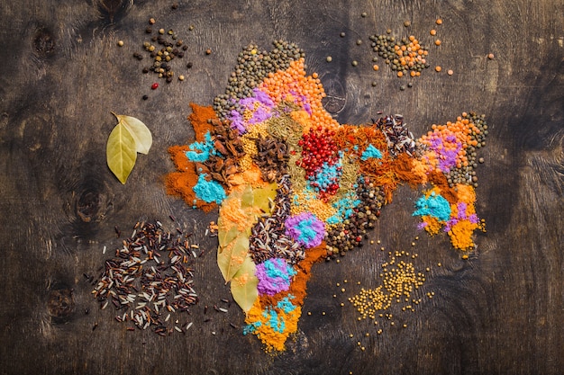 Carte de l'Inde faite de différentes épices indiennes traditionnelles, riz, lentilles et poudre de couleurs Holi sur fond de bois foncé, vue de dessus. Assaisonnements et ingrédients pour cuisiner des plats indiens, concept