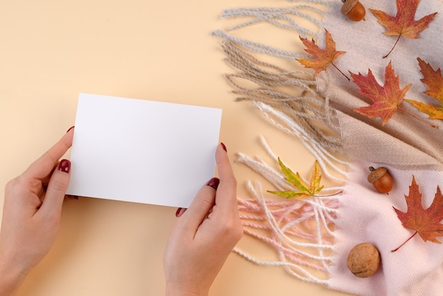 Carte en mains sur fond d'automne - une écharpe, des noix et des feuilles tombées sur fond beige. vue de dessus