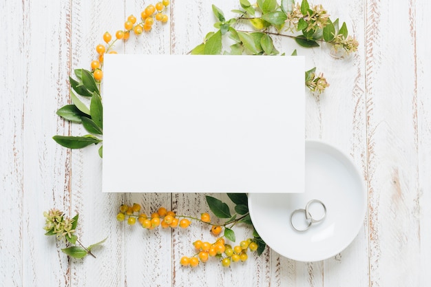 Carte de mariage vierge blanche avec des fleurs; baies jaunes et alliances sur fond en bois