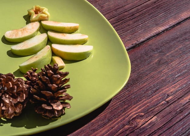 Carte de Noël Un arbre de Noël fait de tranches de pomme verte se trouve sur une plaque verte avec des pommes de pin