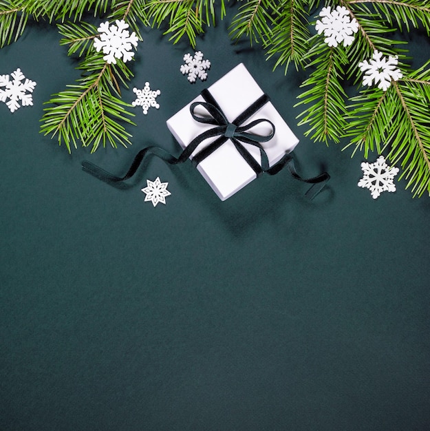 Carte de Noël avec des branches d'arbres de Noël boîte-cadeau blanche flocons de neige blancs sur l'espace de copie vert