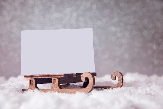 Photo carte de noël sur un traîneau sur la neige. fond festif de paillettes