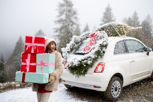 Carte photo de Noël d'une femme avec des cadeaux et une voiture dans les montagnes par temps de neige