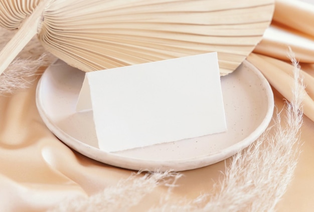 Carte pliée près d'une feuille de palmier séchée et d'un tissu soyeux beige close up salutation ou maquette de mariage