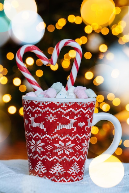 Carte postale de Noël avec une tasse rouge de biscuit de pain d'épice avec l'ornement de Noël sur le bokeh léger de Noël