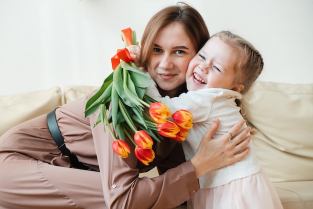 Carte postale pour le 8 mars Petite fille embrasse et étreint sa mère avec des tulipes à fleurs jaunes Fête des mères