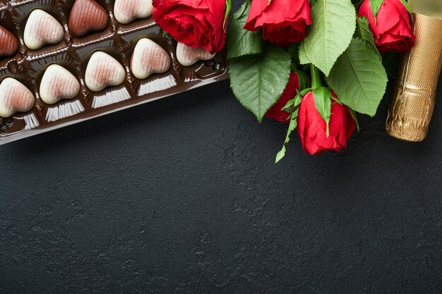 Carte de Saint Valentin Biscuits brownie fleurs rouges roses et bonbons au chocolat sur une boîte cadeau en forme de coeur avec du vin sur fond noir Carte de voeux Fête des mères ou des femmes Vue de dessus plat poser