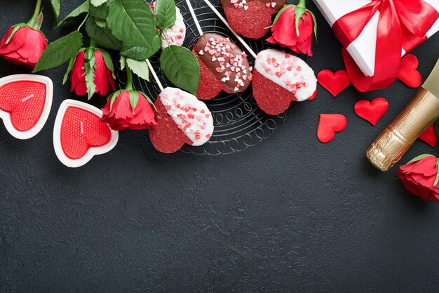 Carte de Saint Valentin Biscuits brownie fleurs rouges roses et bonbons au chocolat sur une boîte cadeau en forme de coeur avec du vin sur fond noir Carte de voeux Fête des mères ou des femmes Vue de dessus plat poser