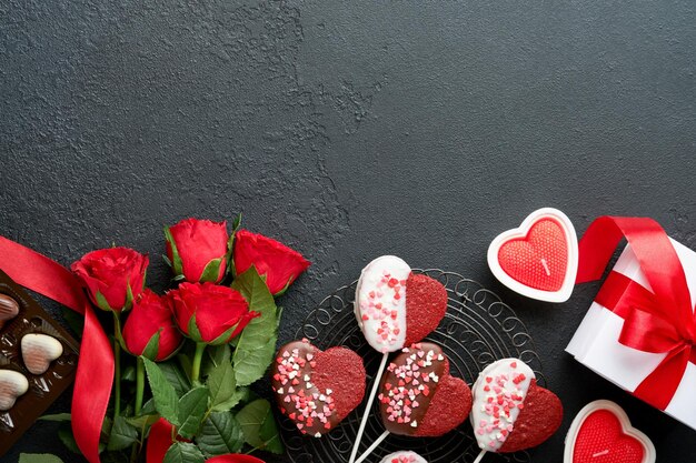 Carte de Saint Valentin Biscuits brownie fleurs rouges roses et bonbons au chocolat sur une boîte cadeau en forme de coeur avec du vin sur fond noir Carte de voeux Fête des mères ou des femmes Vue de dessus plat poser