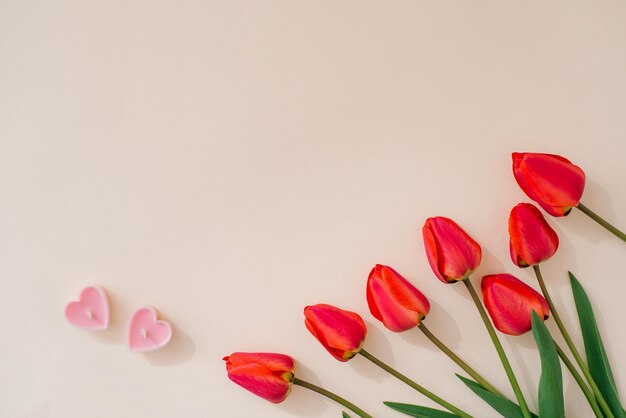 Carte de Saint Valentin avec un bouquet de tulipes rouges et deux bougies coeurs roses sur fond beige avec espace de copie