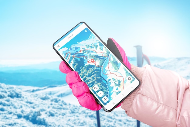 Carte de ski sur l'écran du téléphone à la main avec un gant Bâtons de ski et montagne en arrière-plan