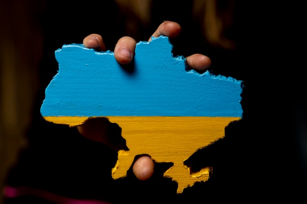 Une carte de l'Ukraine sculptée dans du bois et peinte aux couleurs du drapeau ukrainien entre les mains d'une fille sur fond sombre