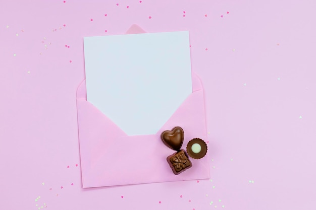 Carte vide blanche avec espace de copie dans une enveloppe rose sur fond rose avec des pralines au chocolat