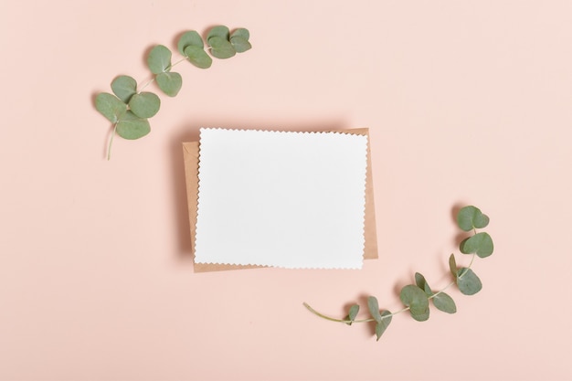 Une carte vierge se trouve sur une enveloppe kraft à côté de deux branches d'eucalyptus. Bannière, invitation, carte postale. Flatlay, Flat lay, Flatly, Vue de dessus, Overhead