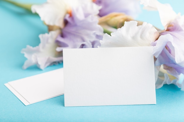 carte de visite blanche avec des fleurs d'iris lilas sur fond bleu pastel. vue latérale, espace de copie