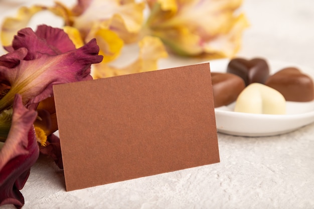 carte de visite brune avec des bonbons au chocolat et des fleurs d'iris sur fond de béton gris. vue de côté