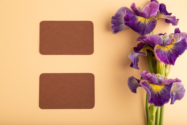 carte de visite brune avec des fleurs d'iris lilas sur fond pastel orange. vue de dessus, mise à plat,