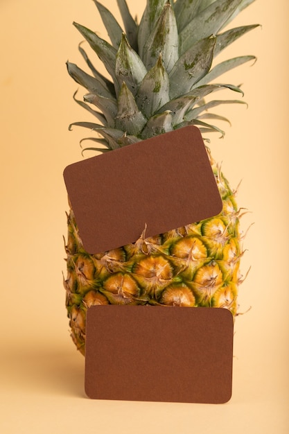 Photo carte de visite en papier brun avec ananas mûr sur fond pastel orange. vue latérale, copiez l'espace.