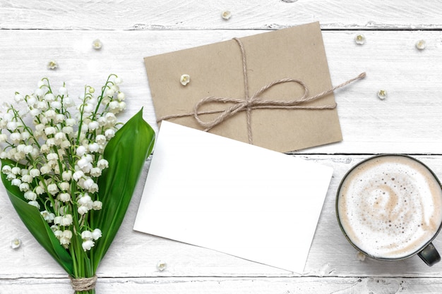 Carte de voeux blanc vierge et enveloppe avec des fleurs de muguet et une tasse de cappuccino