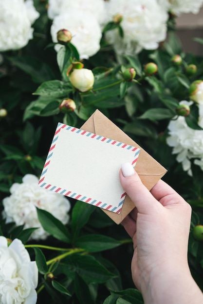 Une carte de vœux blanche et une enveloppe dans la main d'une femme sur un fond floral