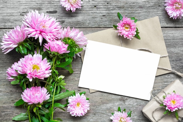 Photo carte de voeux blanche vierge avec bouquet de fleurs d'aster rose et enveloppe avec boutons de fleurs et boîte-cadeau