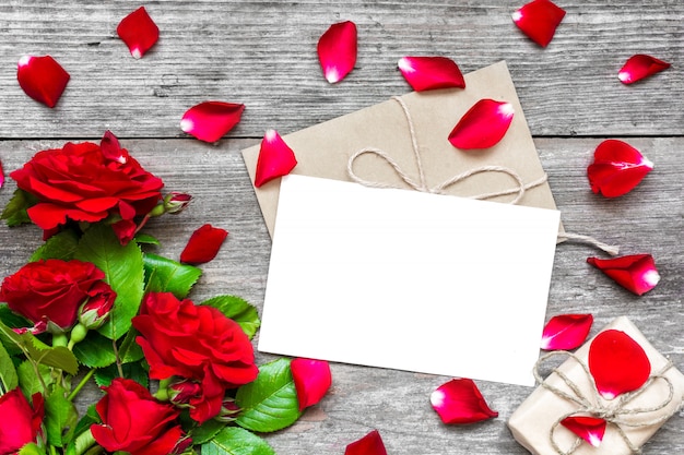Carte de voeux blanche vierge et enveloppe avec des fleurs de roses rouges, pétales et coffret cadeau