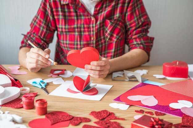 Carte de vœux bricolage avec coeur en papier rouge, symbole de l'amour. La fille fait la fête des mères, la Saint-Valentin, la carte de voeux. Hobby, concept d'art, cadeau de vos propres mains