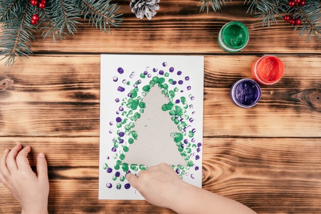 Carte de voeux étape par étape Sapin de Noël avec tutoriel sur les empreintes digitales des enfants. Étape 7 : Trempez le doigt dans une autre peinture et faites des empreintes un peu plus loin. Vue de dessus