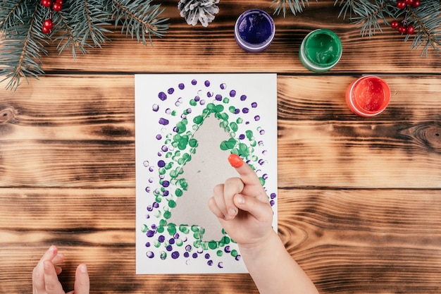 Carte de voeux étape par étape Sapin de Noël avec tutoriel sur les empreintes digitales des enfants. Étape 8 : Trempez votre doigt dans la troisième peinture. Vue de dessus